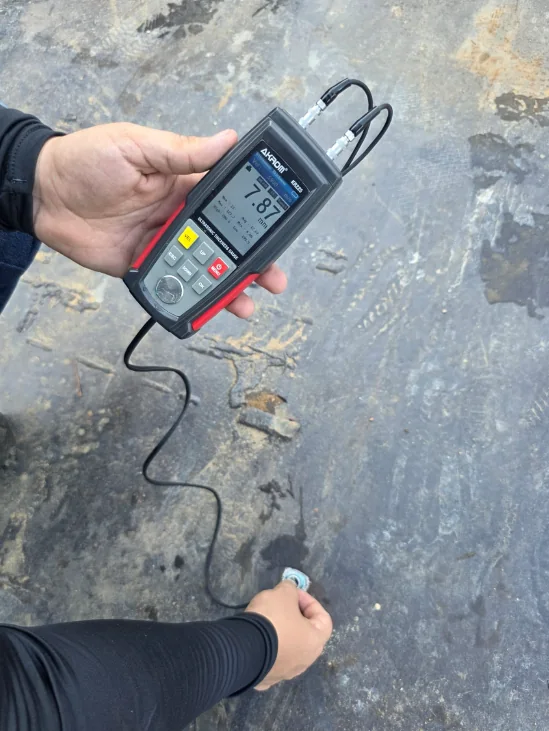 Equipamento de medição de espessura por ultrassom em operação sobre chapeamento metálico